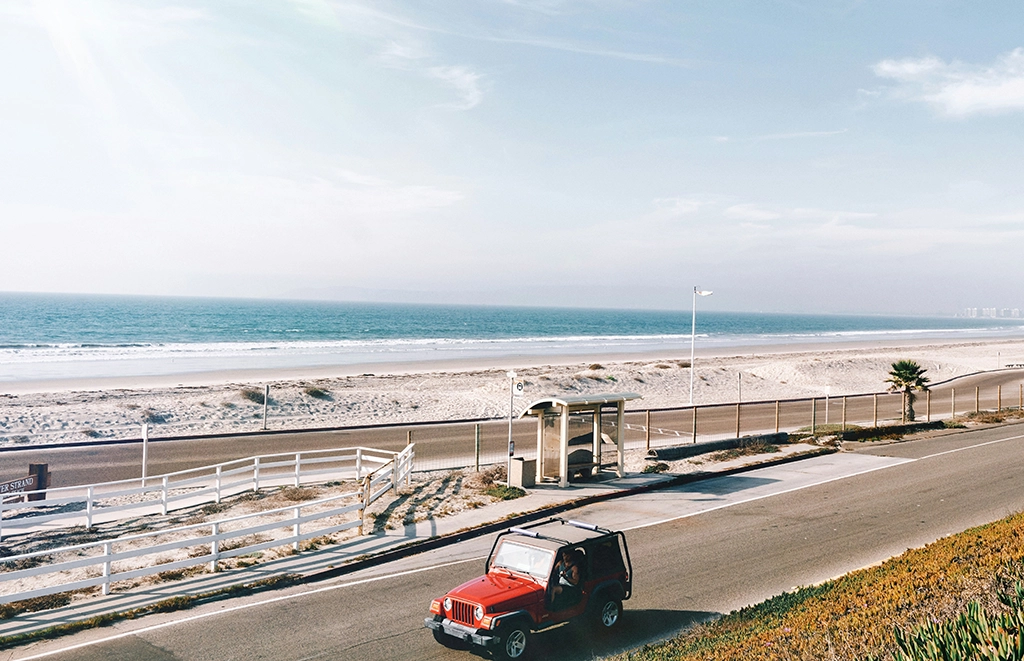 A red jeep driving on a road along the beach in San Diego
